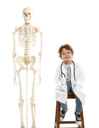 Photo of Choice of profession. Little boy with stethoscope and human skeleton model pretending to be doctor on white background
