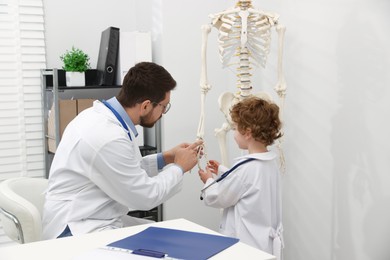 Photo of Choice of profession. Father and his son exploring human skeleton model in clinic