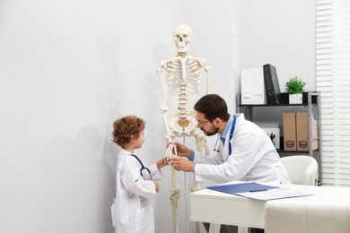 Photo of Choice of profession. Father and his son exploring human skeleton model in clinic