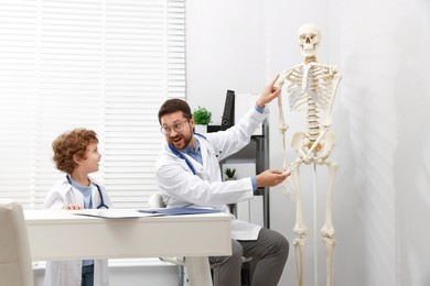 Photo of Choice of profession. Father and his son exploring human skeleton model in clinic