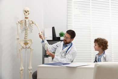 Photo of Choice of profession. Father and his son exploring human skeleton model in clinic