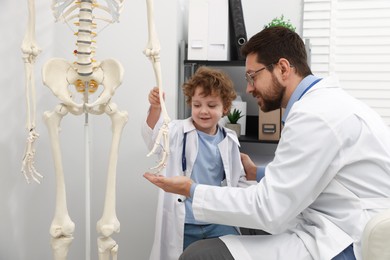 Photo of Choice of profession. Father and his son exploring human skeleton model in clinic