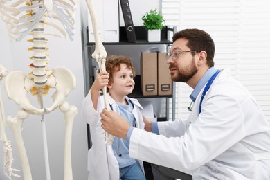 Photo of Choice of profession. Father and his son exploring human skeleton model in clinic