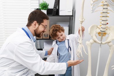 Photo of Choice of profession. Father and his son exploring human skeleton model in clinic