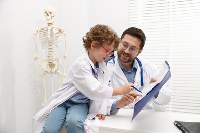 Photo of Choice of profession. Father and his son playing doctor at table in clinic