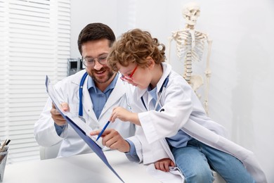 Photo of Choice of profession. Father and his son playing doctor at table in clinic
