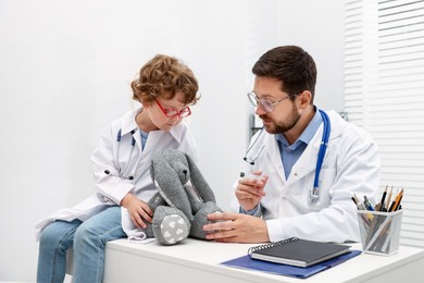 Photo of Choice of profession. Father and his son with toy bunny playing doctor in clinic