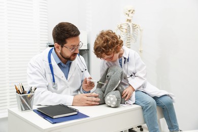 Photo of Choice of profession. Father and his son with toy bunny playing doctor in clinic