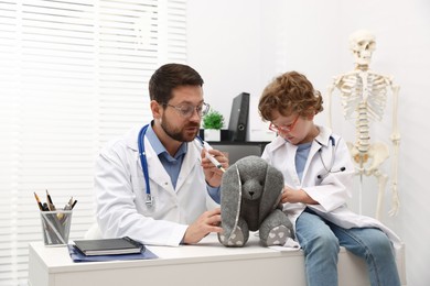 Photo of Choice of profession. Father and his son with toy bunny playing doctor in clinic