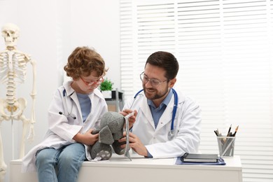 Photo of Choice of profession. Father and his son with toy bunny playing doctor in clinic