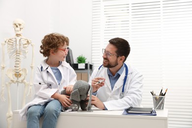 Photo of Choice of profession. Father and his son with toy bunny playing doctor in clinic