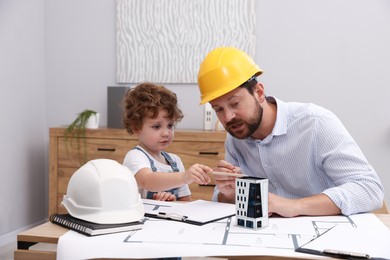 Photo of Choice of profession. Father and his son exploring house model at table indoors