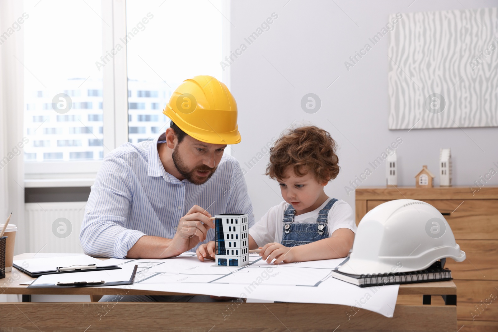 Choice of profession. Father and his son exploring house model at table indoors Photo of Choice of profession. Father and his son exploring house model at table indoors