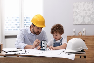 Photo of Choice of profession. Father and his son exploring house model at table indoors