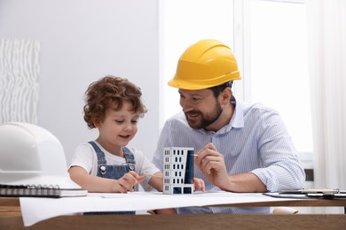 Photo of Choice of profession. Father and his son exploring house model at table indoors