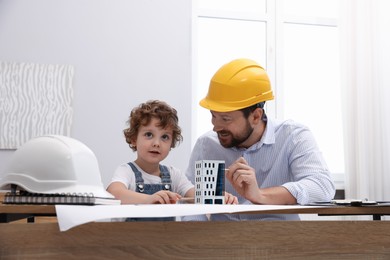 Photo of Choice of profession. Father and his son exploring house model at table indoors