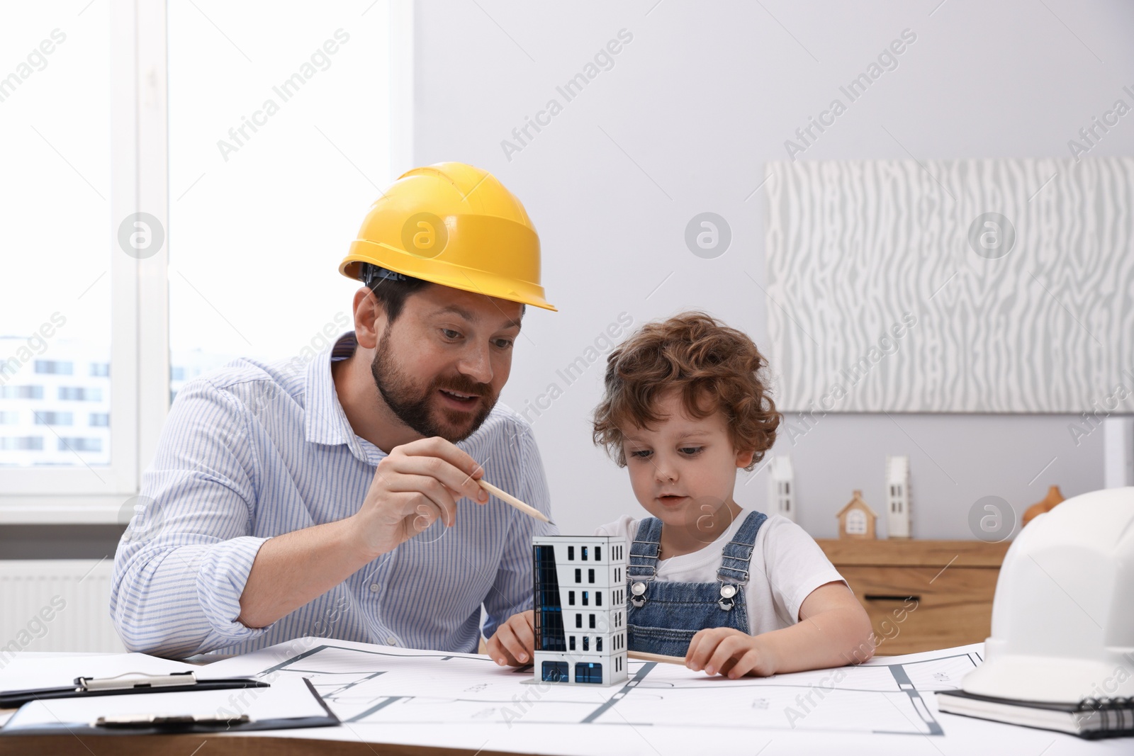 Choice of profession. Father and his son exploring house model at table indoors Photo of Choice of profession. Father and his son exploring house model at table indoors