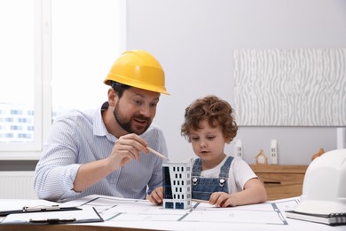 Photo of Choice of profession. Father and his son exploring house model at table indoors