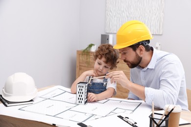 Photo of Choice of profession. Father and his son exploring house model at table indoors