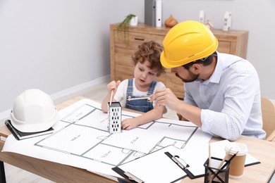 Photo of Choice of profession. Father and his son exploring house model at table indoors