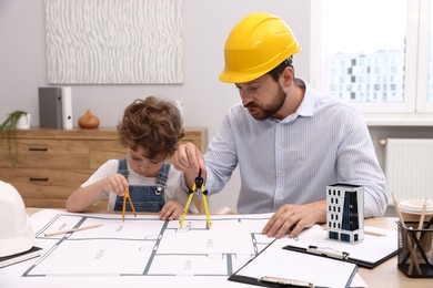 Photo of Choice of profession. Father and his son with dividers exploring engineering drawings at table indoors