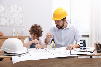 Photo of Choice of profession. Father and his son with dividers exploring engineering drawings at table indoors