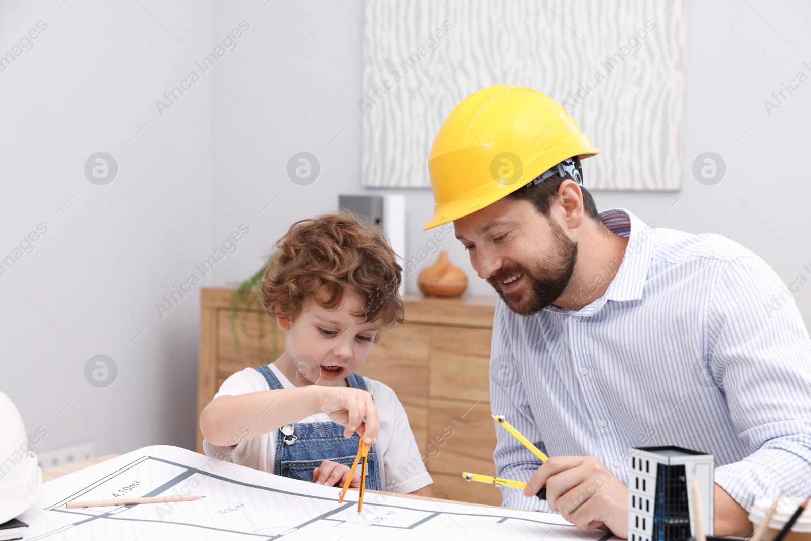 Choice of profession. Father and his son with dividers exploring engineering drawings at table indoors Photo of Choice of profession. Father and his son with dividers exploring engineering drawings at table indoors