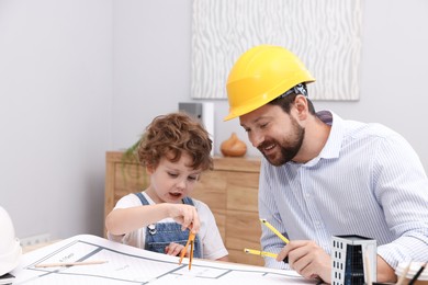 Photo of Choice of profession. Father and his son with dividers exploring engineering drawings at table indoors
