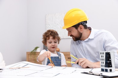 Photo of Choice of profession. Father and his son with dividers exploring engineering drawings at table indoors