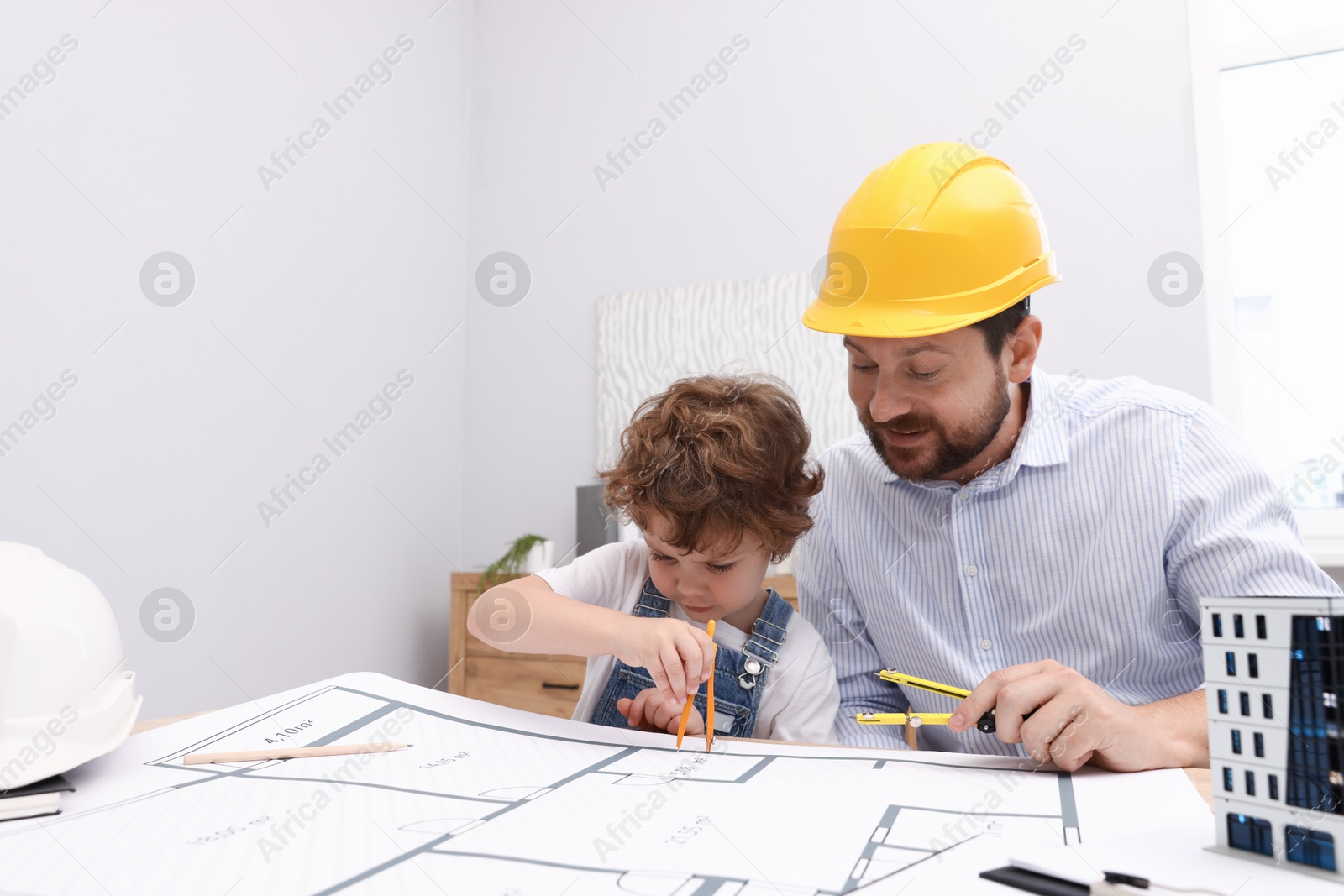 Choice of profession. Father and his son with dividers exploring engineering drawings at table indoors Photo of Choice of profession. Father and his son with dividers exploring engineering drawings at table indoors