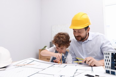 Photo of Choice of profession. Father and his son with dividers exploring engineering drawings at table indoors
