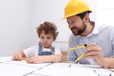 Photo of Choice of profession. Father and his son with dividers exploring engineering drawings at table indoors