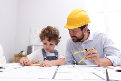 Photo of Choice of profession. Father and his son with dividers exploring engineering drawings at table indoors