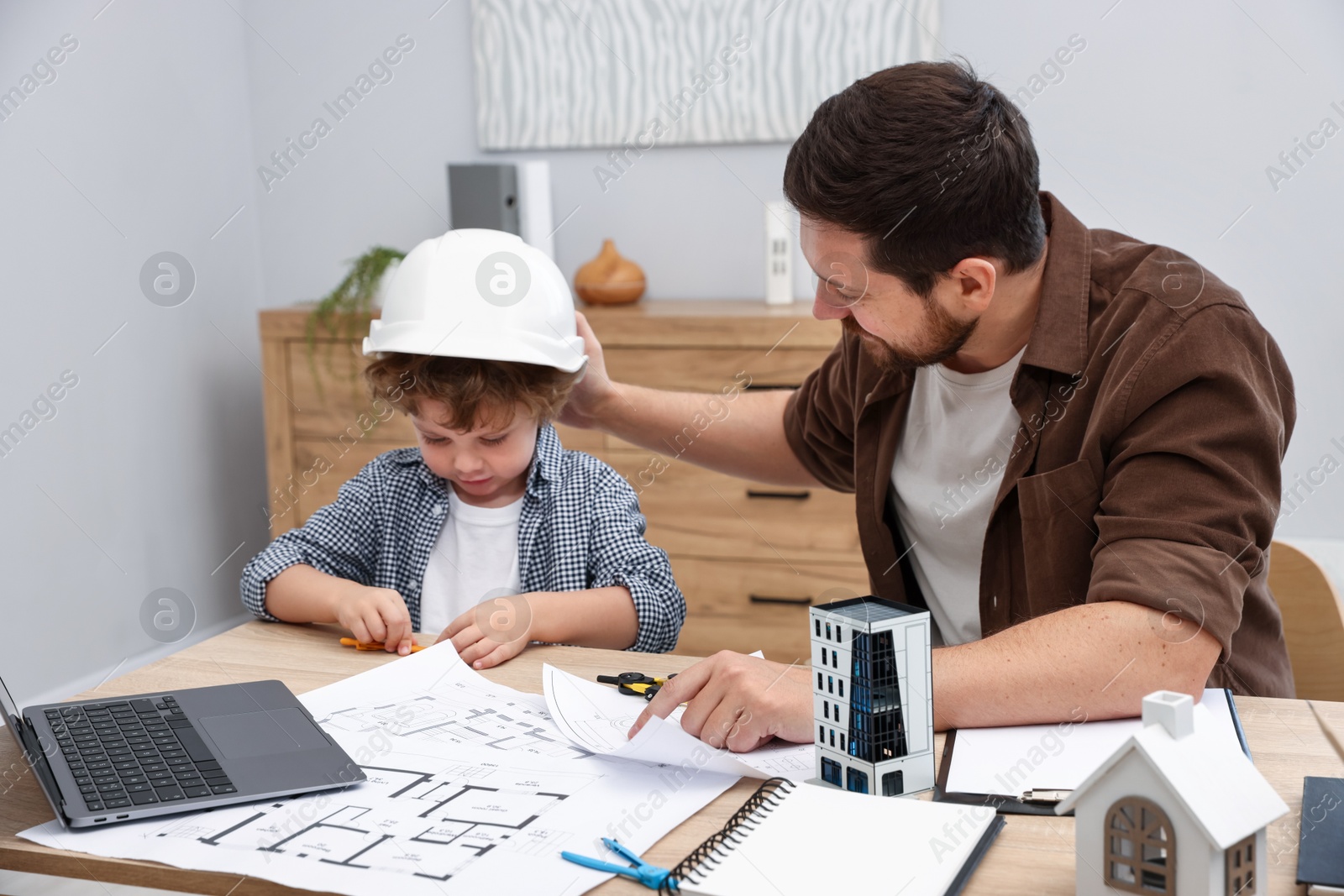 Choice of profession. Father and his son at table with laptop and engineering drawings indoors Photo of Choice of profession. Father and his son at table with laptop and engineering drawings indoors
