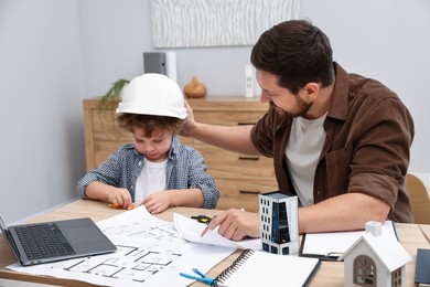 Photo of Choice of profession. Father and his son at table with laptop and engineering drawings indoors