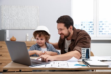 Photo of Choice of profession. Father and his son at table with laptop and engineering drawings indoors