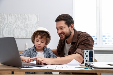 Photo of Choice of profession. Father and his son at table with laptop and engineering drawings indoors