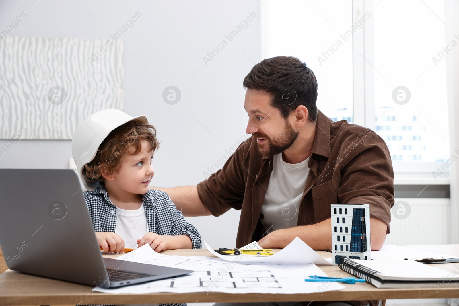 Choice of profession. Father and his son at table with laptop and engineering drawings indoors Photo of Choice of profession. Father and his son at table with laptop and engineering drawings indoors