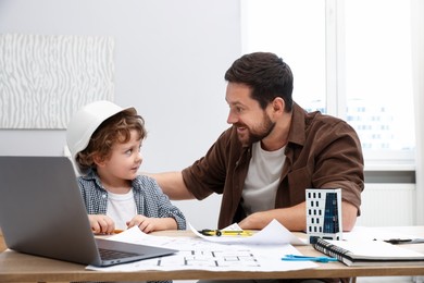 Photo of Choice of profession. Father and his son at table with laptop and engineering drawings indoors
