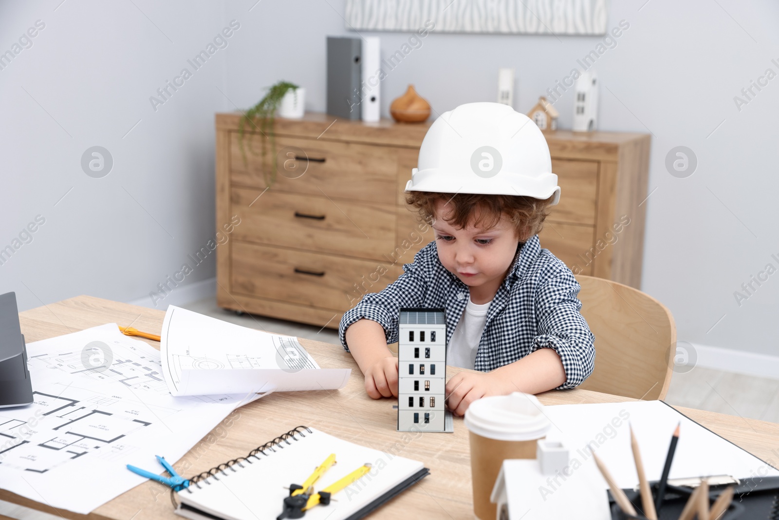 Choice of profession. Little kid in hard hat exploring house model at table indoors Photo of Choice of profession. Little kid in hard hat exploring house model at table indoors