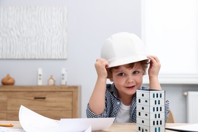 Photo of Choice of profession. Little kid in hard hat pretending to be engineer at table indoors