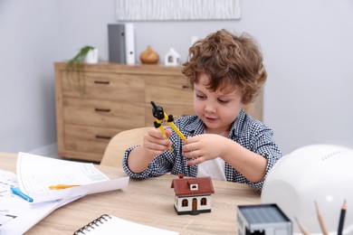 Photo of Choice of profession. Little kid with divider pretending to be engineer at table indoors