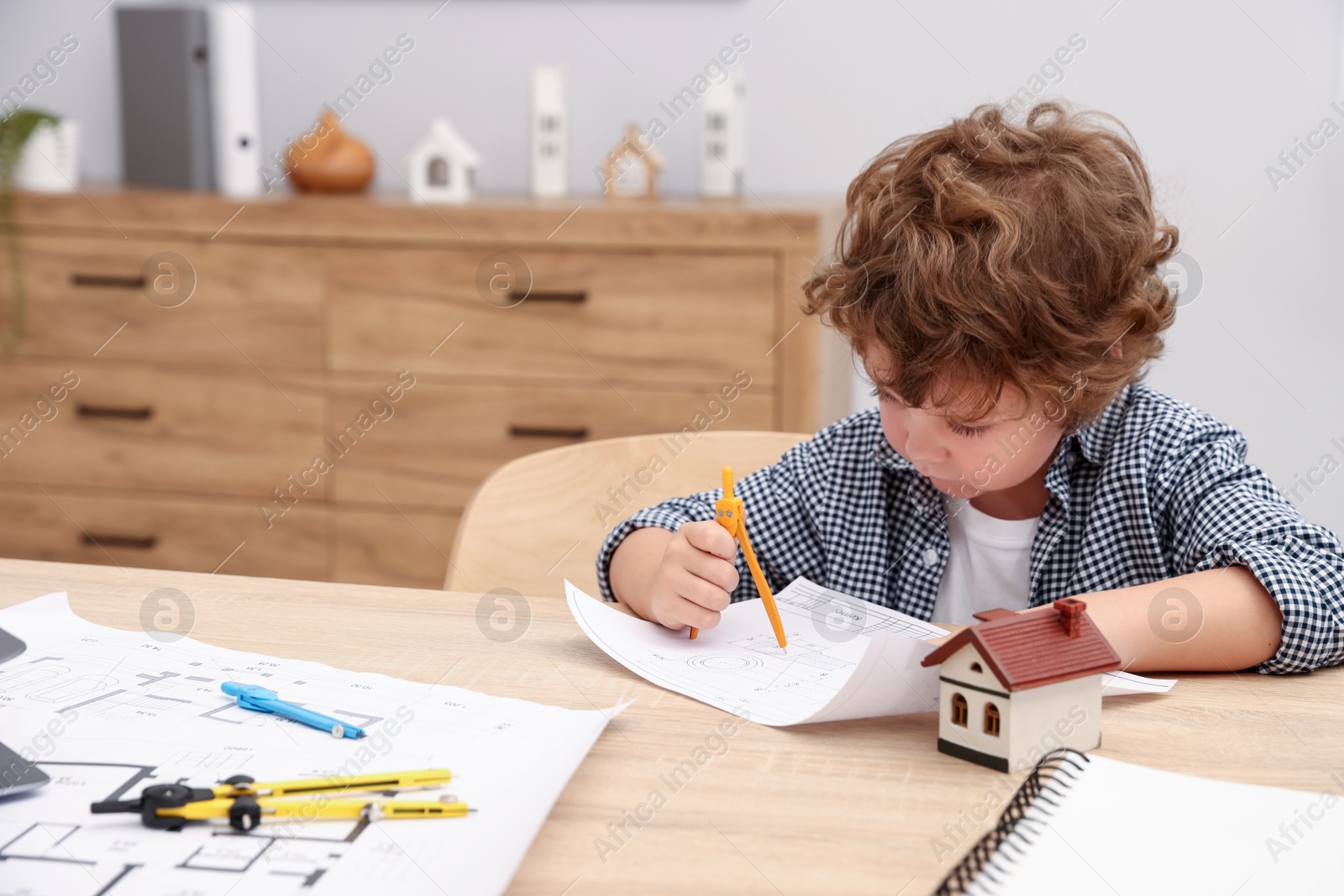 Choice of profession. Little kid with divider and engineering drawing at table indoors Photo of Choice of profession. Little kid with divider and engineering drawing at table indoors
