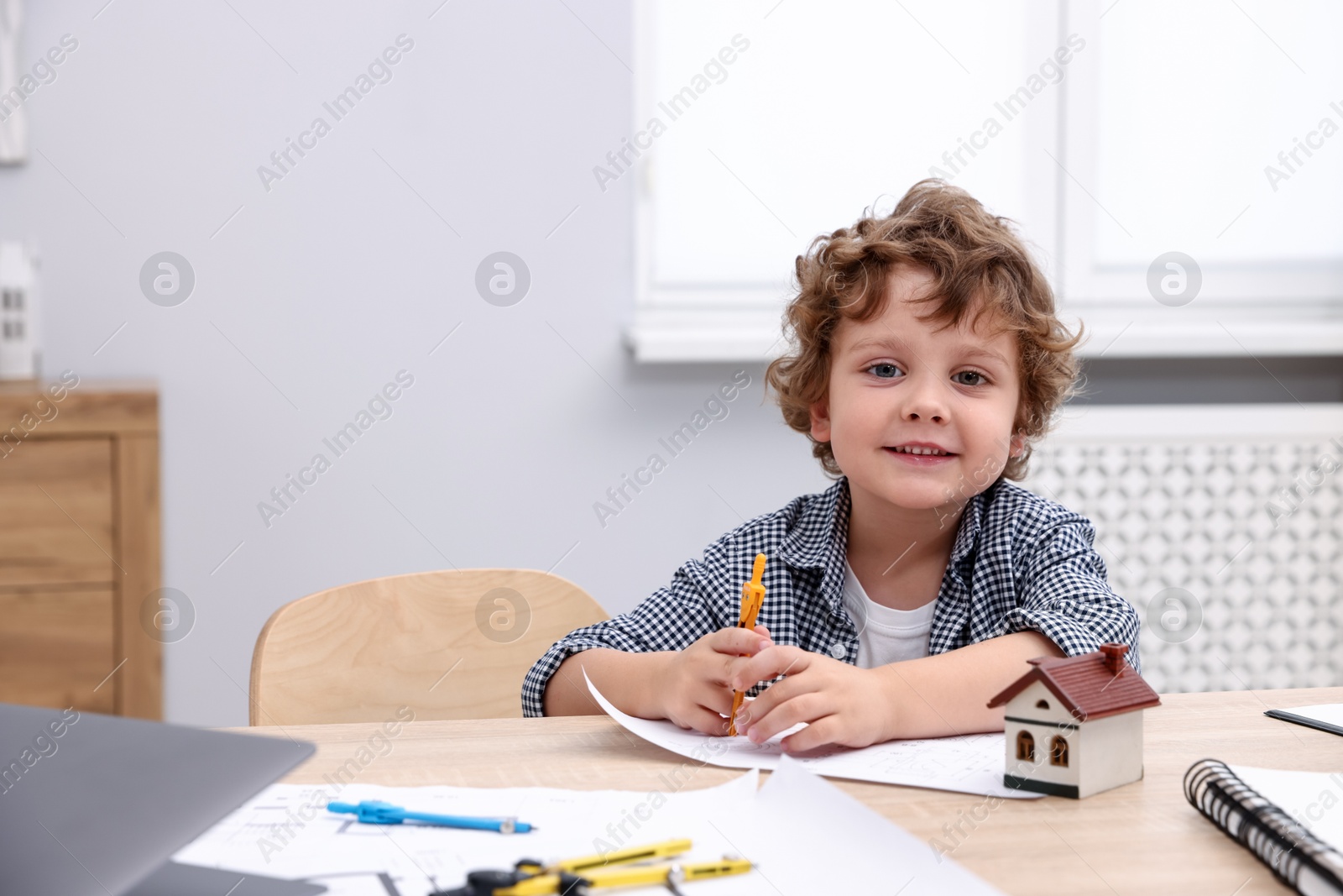 Choice of profession. Little kid with divider and engineering drawing at table indoors Photo of Choice of profession. Little kid with divider and engineering drawing at table indoors