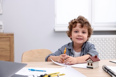 Photo of Choice of profession. Little kid with divider and engineering drawing at table indoors