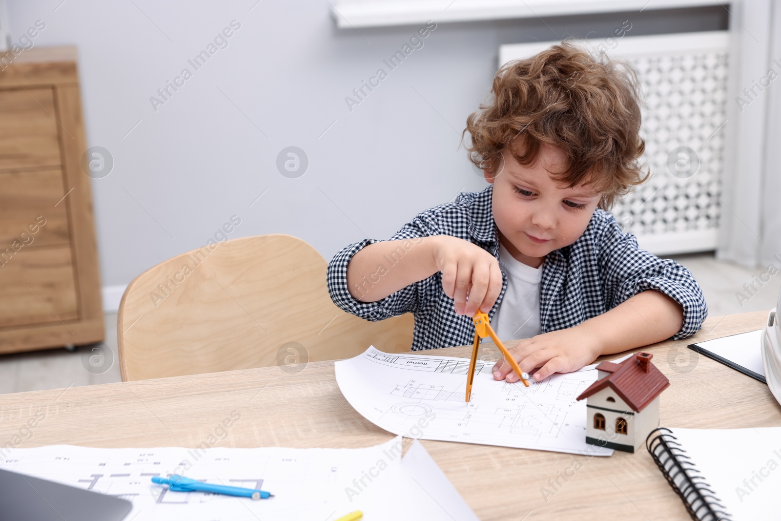 Choice of profession. Little kid with divider and engineering drawing at table indoors Photo of Choice of profession. Little kid with divider and engineering drawing at table indoors