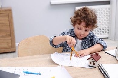 Photo of Choice of profession. Little kid with divider and engineering drawing at table indoors