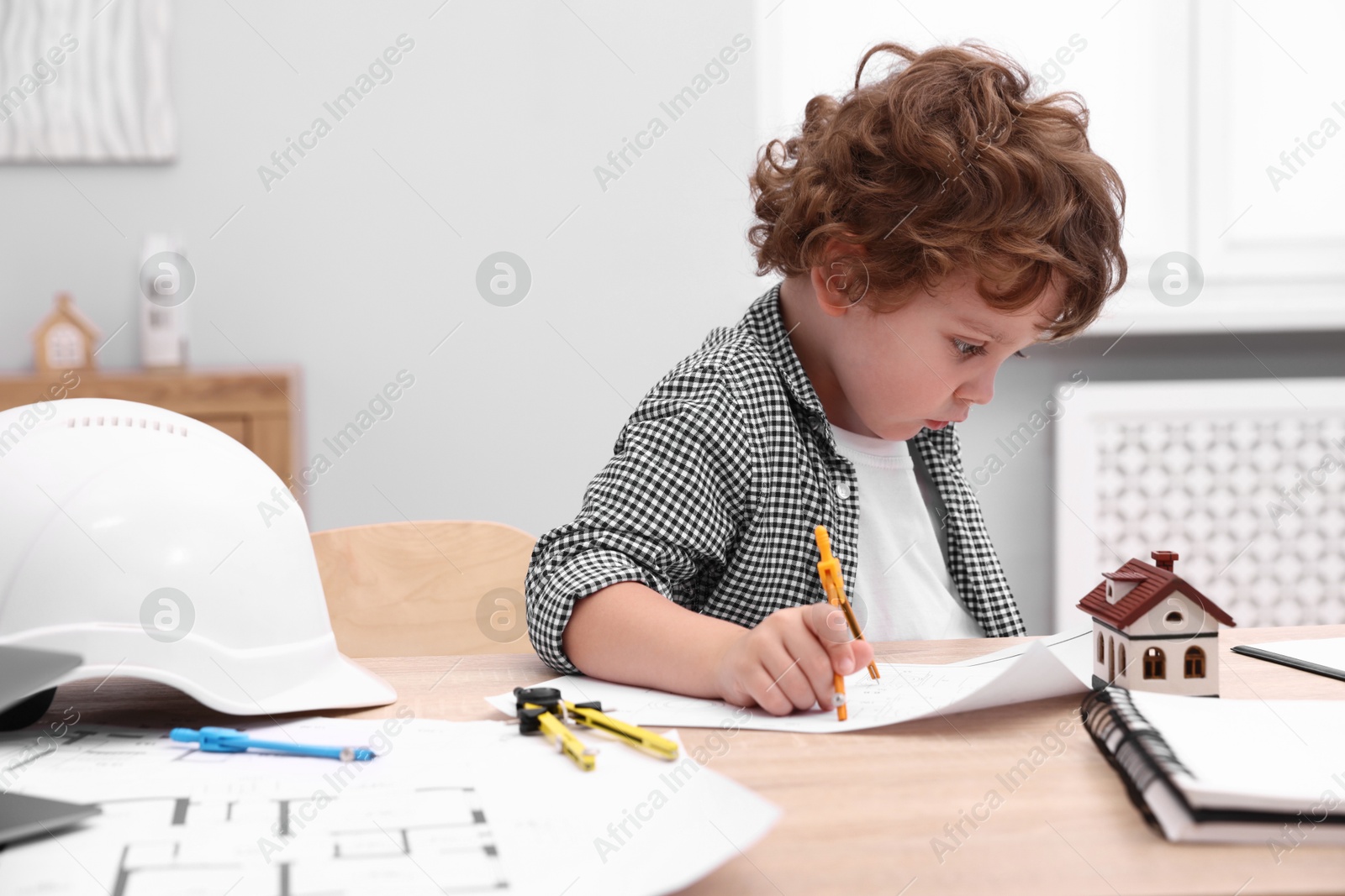 Choice of profession. Little kid with divider and engineering drawing at table indoors Photo of Choice of profession. Little kid with divider and engineering drawing at table indoors