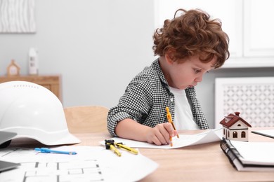 Photo of Choice of profession. Little kid with divider and engineering drawing at table indoors