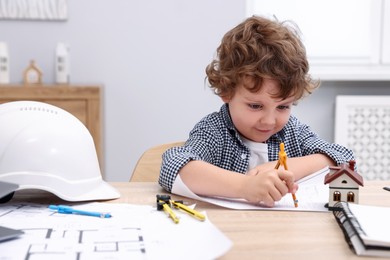 Photo of Choice of profession. Little kid with divider and engineering drawing at table indoors
